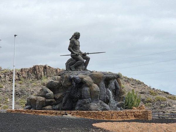 Imposante Statue des Mencey Tinerfe, eines Guanchenkönigs, auf einem Felsen mit Wasserfall – ein Symbol der Geschichte von Teneriffa.