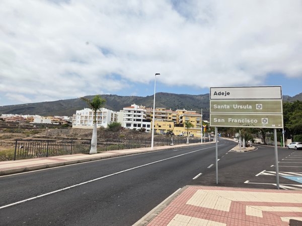 Ein Straßenschild in Adeje zeigt die Richtung nach Santa Ursula und San Francisco. Im Hintergrund sind Wohngebäude und die Berge sichtbar.