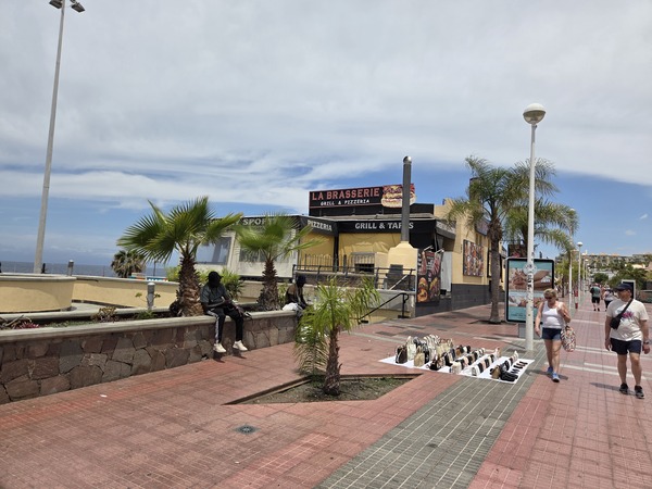 Spaziergänger an der Strandpromenade von Playa Fañabé mit Palmen und Restaurants im Hintergrund